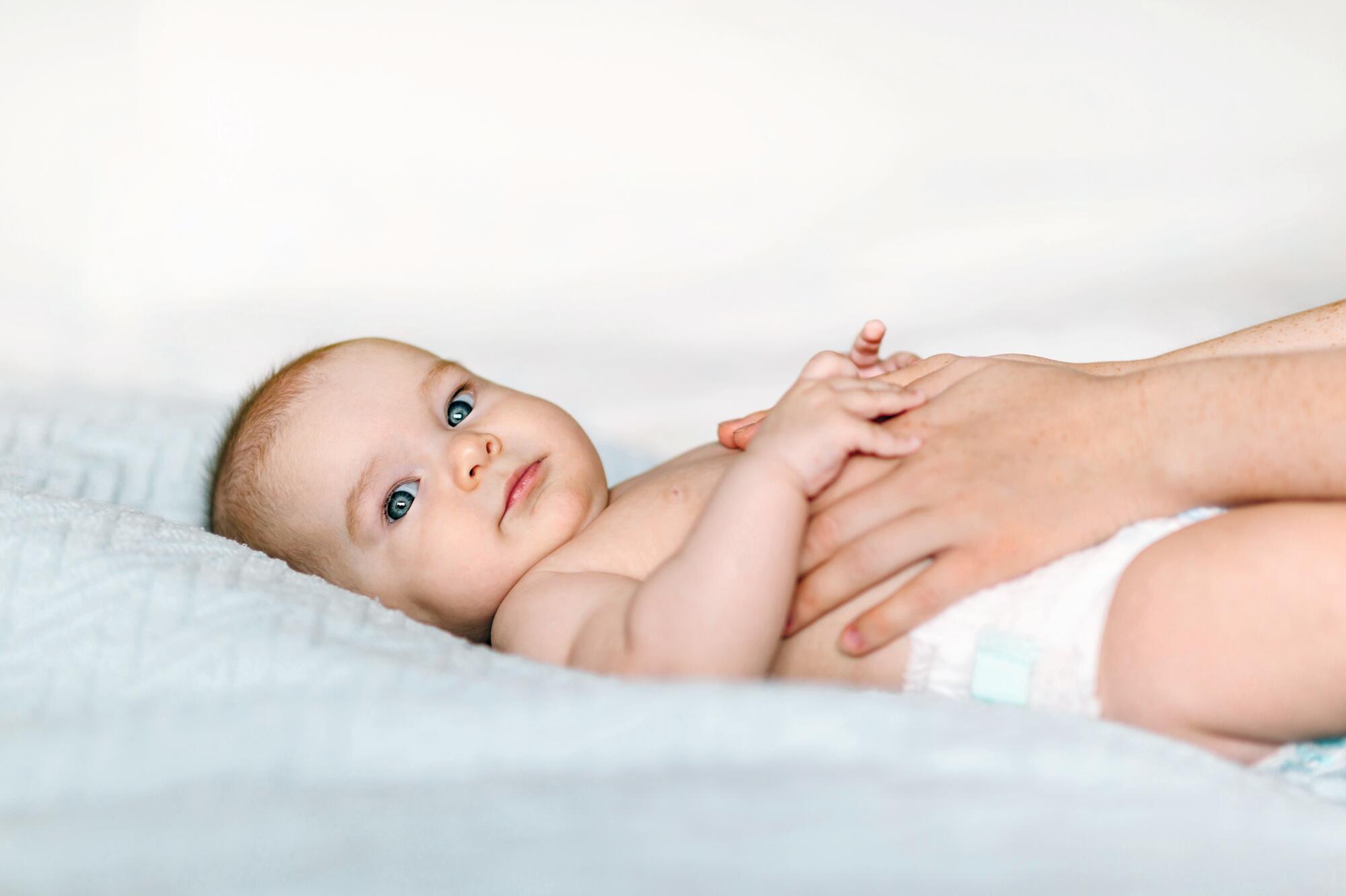 Baby ligger på et underlag og får omsorg fra en voksen.